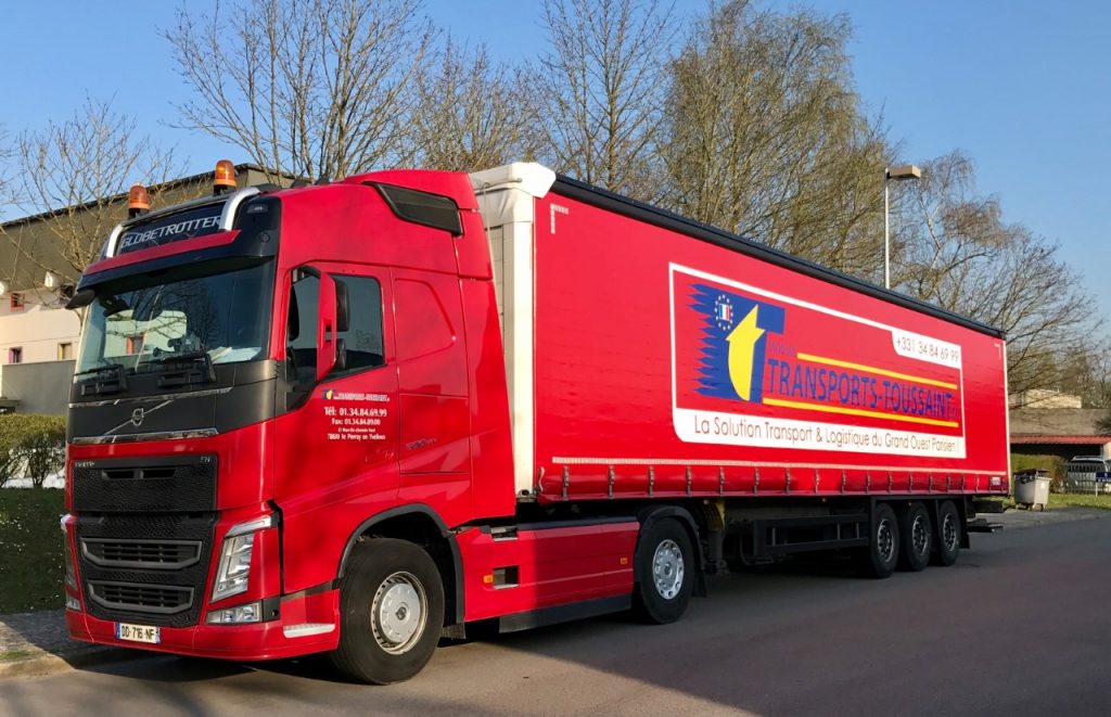 Camion Volvo FH Globetrotter (très probablement un FH 500) rouge de Transports Toussaint stationné à Le Perray-en-Yvelines, affichant leur logo, numéro de téléphone et slogan "La Solution Transport & Logistique du Grand Ouest Parisien !", illustrant leurs services de transport routier régional, national et international.