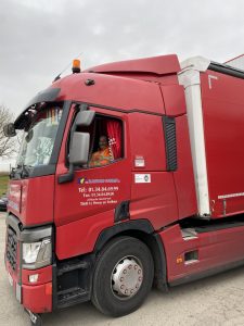 Chauffeur souriant au volant d'un camion rouge Renault Trucks T (possiblement un T 440) de Transports Toussaint à Le Perray-en-Yvelines, affichant leurs coordonnées et soulignant l'humain au cœur de leur service de transport routier en Île-de-France.