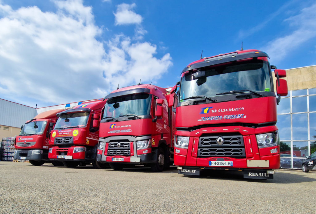 Alignement de camions rouges Transports Toussaint stationnés devant un entrepôt logistique